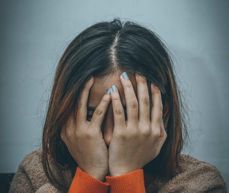 woman in brown sweater covering her face with her hand